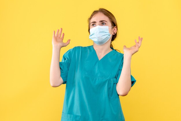 Medico femminile vista frontale in maschera su sfondo giallo pandemia covid- ospedale