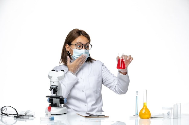 Medico femminile vista frontale in tuta medica bianca con maschera a causa di covid lavorando con soluzioni su uno spazio bianco