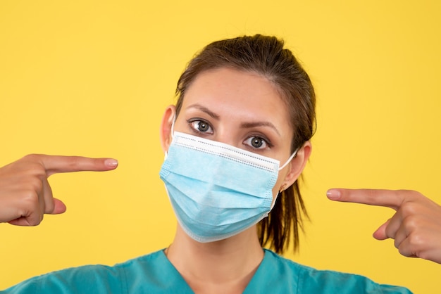 Medico femminile vista ravvicinata anteriore in maschera sterile su sfondo giallo