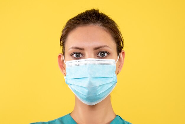 Medico femminile vista ravvicinata anteriore in maschera sterile su sfondo giallo