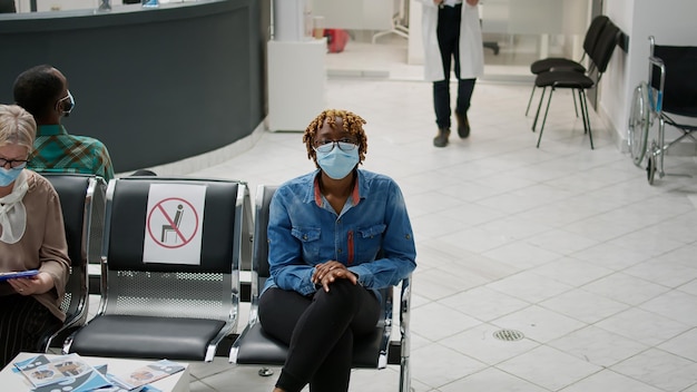 Medico generico che invita il paziente in studio medico per la visita di controllo, in attesa alla reception dell'ospedale durante la pandemia di coronavirus. Medico e donna con maschera facciale che si consultano in clinica.