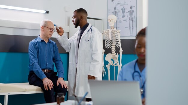 Medico generico che utilizza il termometro per controllare la febbre sul paziente anziano in studio medico. Medico maschio che esegue la misurazione della temperatura durante la consultazione sanitaria con l'uomo anziano, visita di controllo.