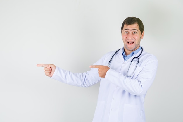 Medico maschio che indica le dita a lato in camice bianco e guardando eccitato