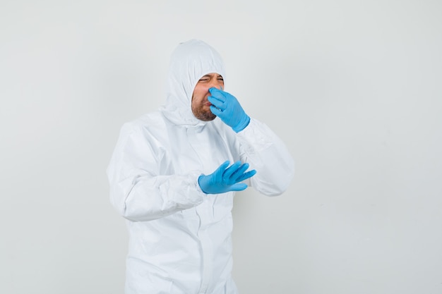Medico maschio che pizzica il naso a causa del cattivo odore in tuta protettiva