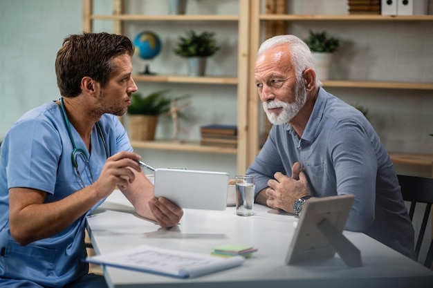 Medico maschio che utilizza il touchpad e spiega i risultati dei test medici al suo paziente anziano durante l'appuntamento medico