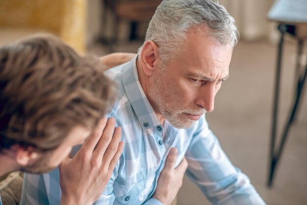 Medico maschio dai capelli scuri che si occupa di un uomo dalla testa grigia grave e sconvolto che soffre di un dolore al petto