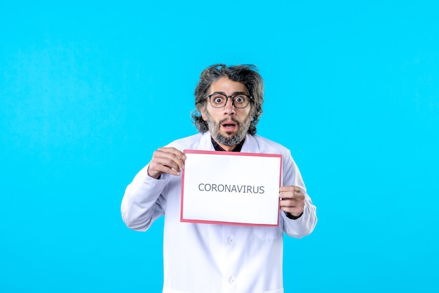 Medico maschio di vista frontale che tiene la scrittura del coronavirus sul blu