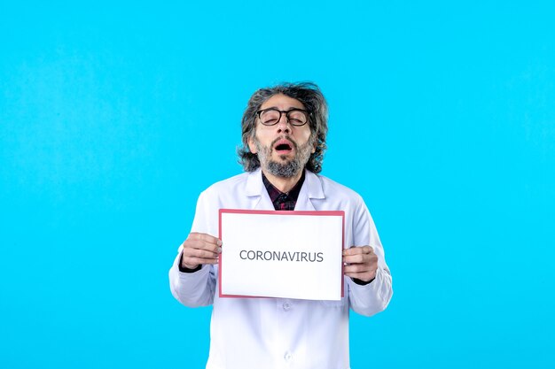 Medico maschio di vista frontale che tiene la scrittura del coronavirus sul blu