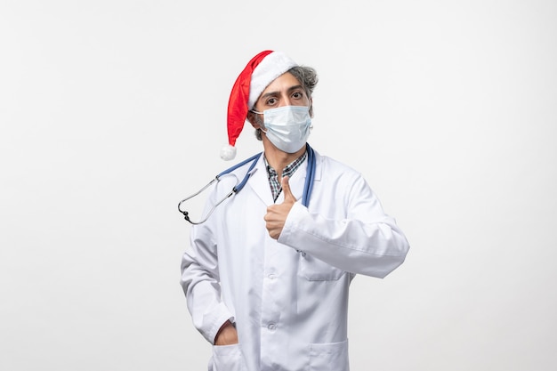Medico maschio di vista frontale in maschera sterile sulla pandemia del nuovo anno del virus covid della parete bianca
