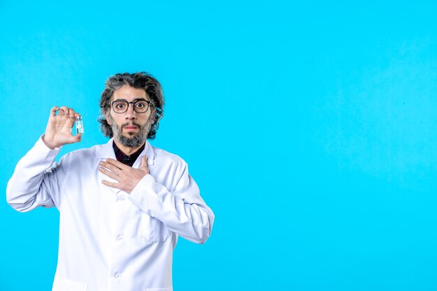 Medico maschio di vista frontale in uniforme medica che tiene piccola boccetta su un virus dell'ospedale blu scienza del colore covid- malattia sanitaria pandemia