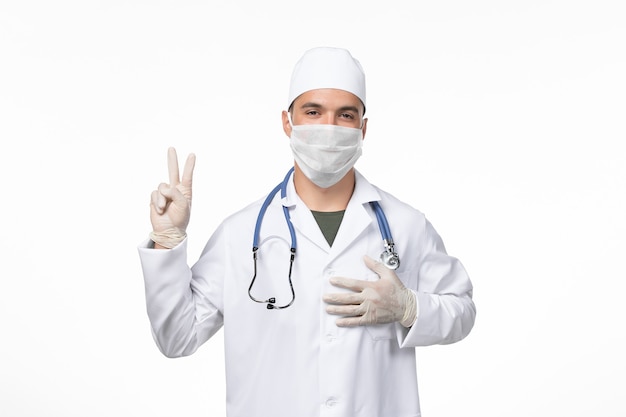 Medico maschio di vista frontale in vestito medico e maschera da portare a causa della malattia covid del virus della malattia della scrivania leggera