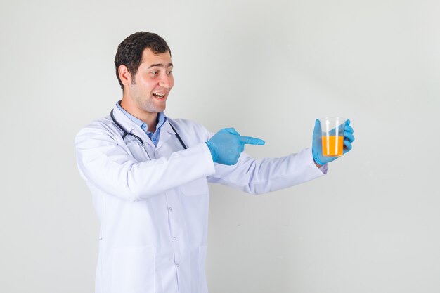 Medico maschio in camice bianco, guanti che indicano il dito al bicchiere di succo e che sembra allegro