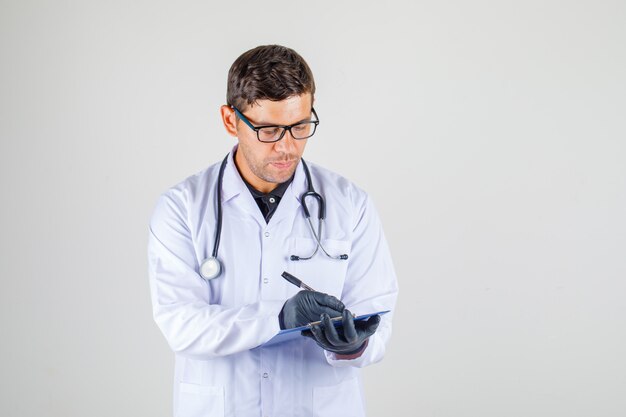 Medico maschio nella prescrizione medica bianca di scrittura dell'abito