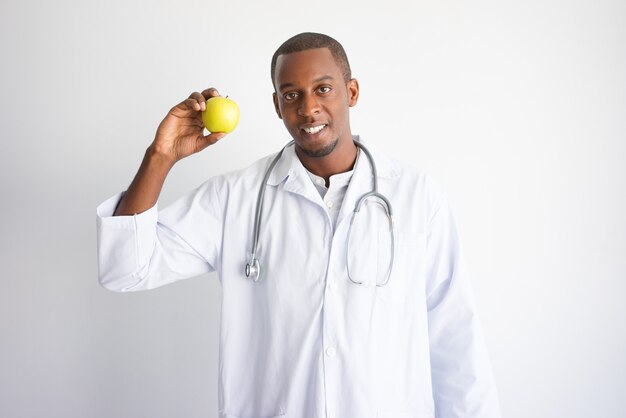 Medico maschio nero sorridente che mostra e che raccomanda mela.