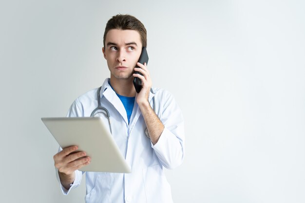 Medico maschio pensieroso che utilizza computer tablet e smartphone