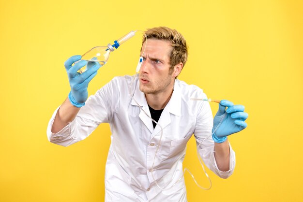 Medico maschio vista frontale che tiene contagocce su sfondo giallo medico pandemia umana covid