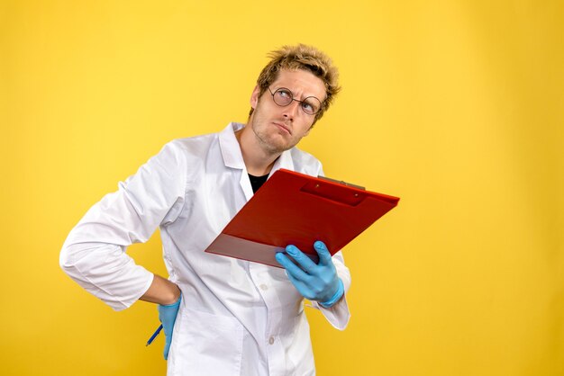 Medico maschio vista frontale con note e penna su sfondo giallo salute covid- medico umano