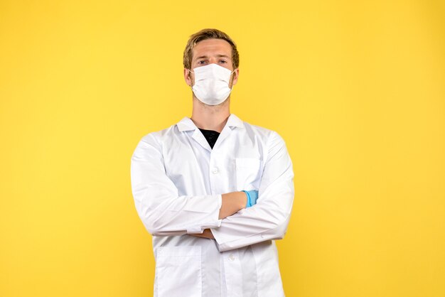 Medico maschio vista frontale in maschera su sfondo giallo virus salute covid- pandemia