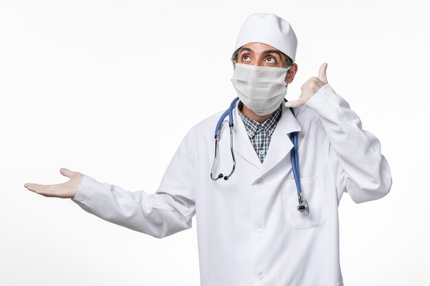 Medico maschio vista frontale in tuta medica con maschera a causa di covid sulla superficie bianca