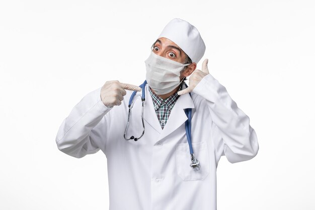 Medico maschio vista frontale in tuta medica con maschera a causa di covid sulla superficie bianca