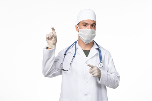 Medico maschio vista frontale in tuta medica e indossa una maschera contro covid sul virus pandemico della medicina della malattia di covid della parete bianca