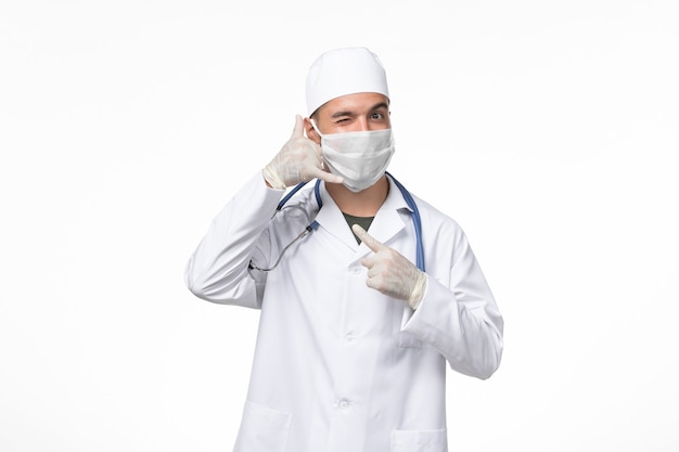 Medico maschio vista frontale in tuta medica e indossa una maschera contro covid sulla scrivania bianca virus pandemico della medicina covid