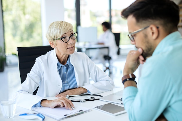 Medico maturo che comunica con il suo paziente mentre analizza i suoi dati medici presso la clinica