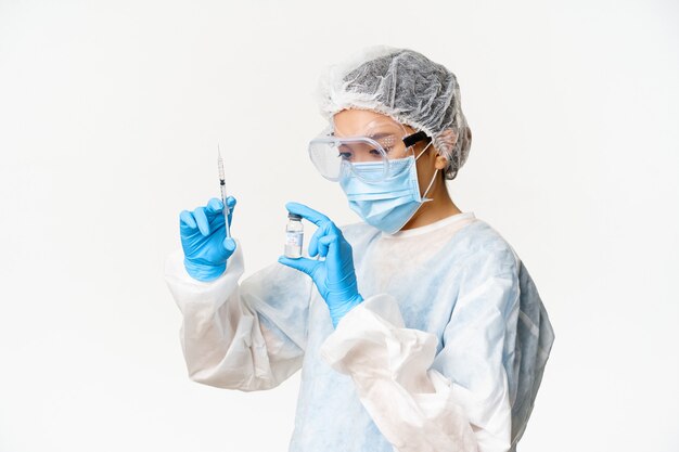 Medico o infermiere donna asiatica in dispositivi di protezione individuale, maschera medica e guanti, riempiendo la siringa con il vaccino covid-19, vaccinando i pazienti, sfondo bianco.