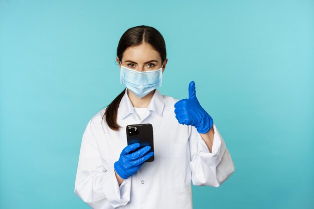 Medico online e clinica giovane donna in maschera medica che utilizza smartphone per client remoto online ...