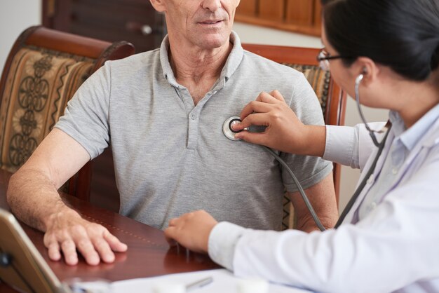 Medico potato che controlla il battito cardiaco del paziente senior