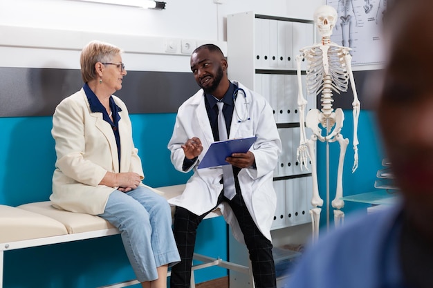 Medico specialista medico che spiega la diagnosi della malattia discutendo il trattamento farmacologico con una donna anziana in pensione nell'ufficio dell'ospedale. Uomo del terapeuta che lavora al recupero medico del paziente. Concetto di medicina