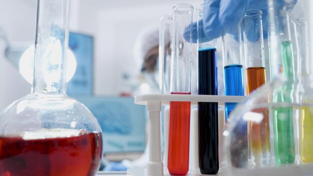 Medico specialista scienziato con attrezzatura PPE che lavora con provette mediche trasparenti che analizzano la soluzione liquida durante l'esperimento di chimica nel laboratorio ospedaliero. Concetto di medicina