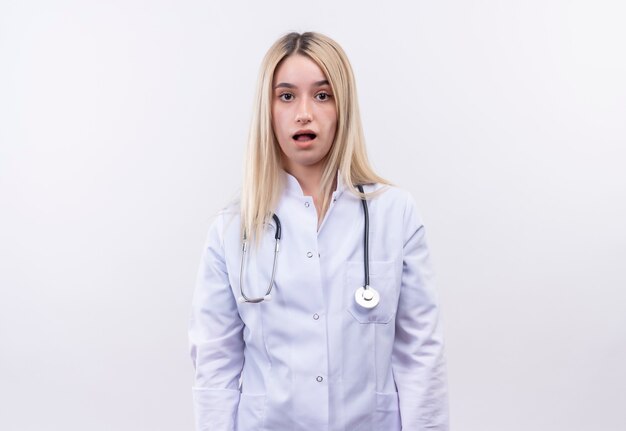 medico stanco giovane ragazza bionda che indossa stetoscopio e camice medico sul muro bianco isolato