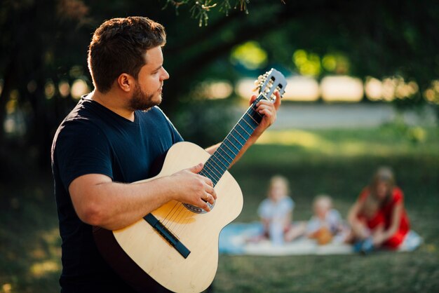 Medium shot lateralmente padre a suonare la chitarra