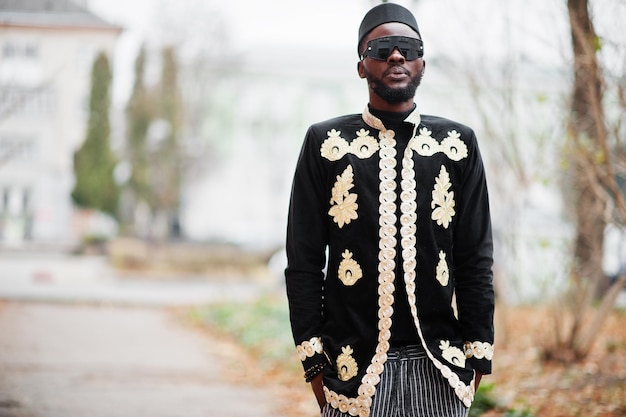 Mega uomo africano alla moda in giacca tradizionale posa Ragazzo nero alla moda con cappello e occhiali da sole