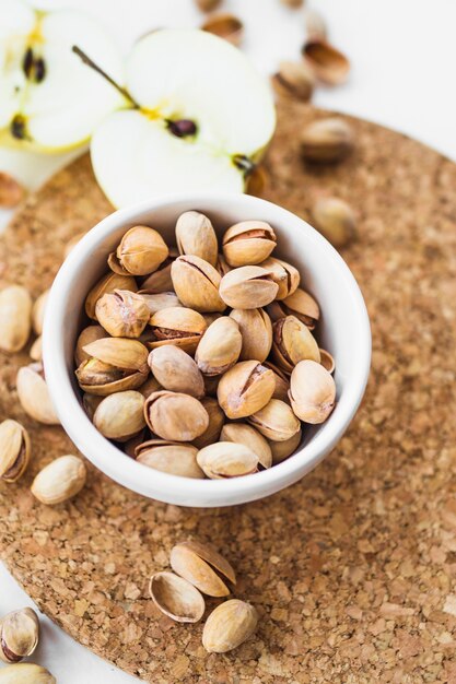 Mela con una ciotola di pistacchi sul sottobicchiere di sughero