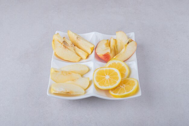 Mela cotogna affettata, mela, pere e limone su un piatto sul tavolo di marmo.