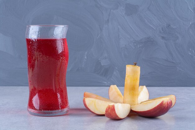 Mela intera e affettata accanto a un bicchiere di succo di ciliegia, sul tavolo di marmo.