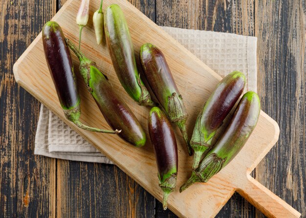 Melanzane con i peperoni sul tagliere sull'asciugamano di cucina e di legno, disposizione piana.