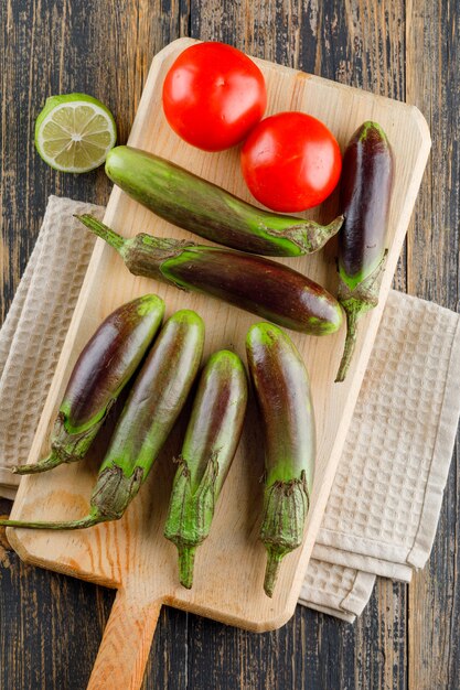 Melanzane con i pomodori, calce sul tagliere sull'asciugamano di legno e della cucina, disposizione piana.