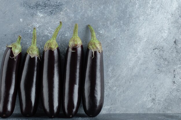 Melanzane fresche organiche in fila su sfondo grigio.