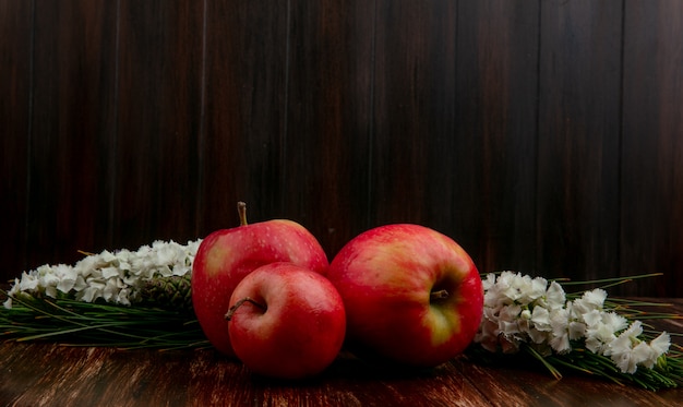 Mele rosse di vista frontale con i fiori bianchi su un fondo di legno