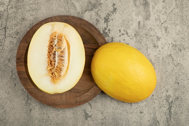 Melone giallo delizioso diviso in due e intero sul piatto di legno.