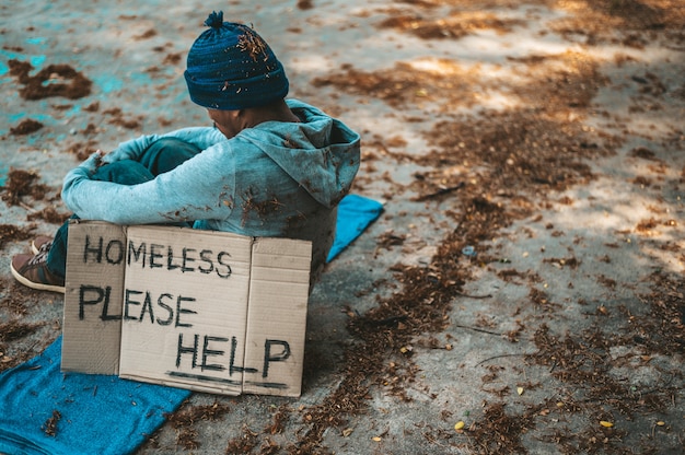 Mendicanti seduti per strada con messaggi per senzatetto, per favore, aiutatemi.