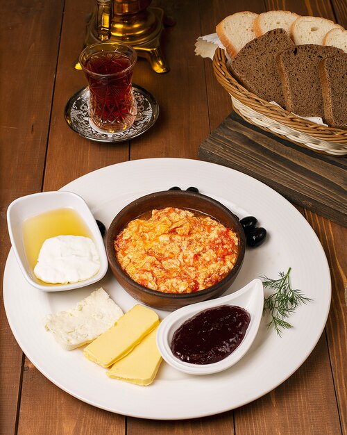 Menemen turco della prima colazione con variazioni del miele, della crema, delle olive, della marmellata e del formaggio in zolla bianca e vetro di tè
