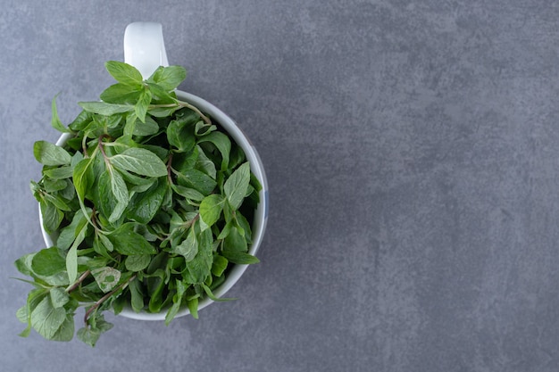 Menta cruda in una tazza, sulla superficie di marmo.