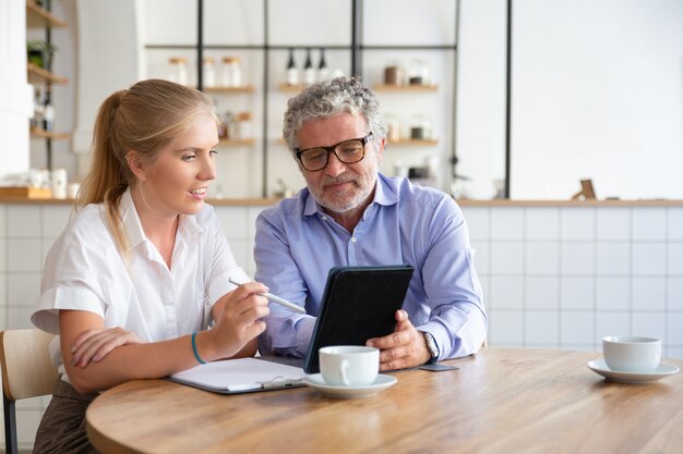 Mentore maschio maturo positivo che spiega i dettagli del lavoro allo stagista