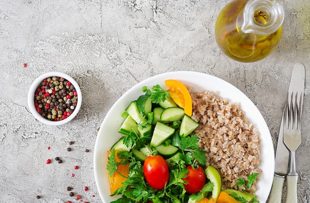 Menu dietetico. Insalata vegetariana sana degli ortaggi freschi - pomodori, cetriolo, peperoni dolci e porridge sulla ciotola. Cibo vegano. Disteso. Vista dall'alto