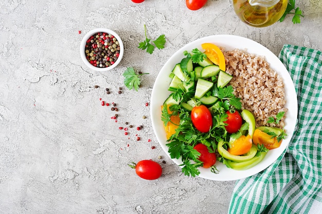 Menu dietetico. Insalata vegetariana sana degli ortaggi freschi - pomodori, cetriolo, peperoni dolci e porridge sulla ciotola. Cibo vegano. Disteso. Vista dall'alto