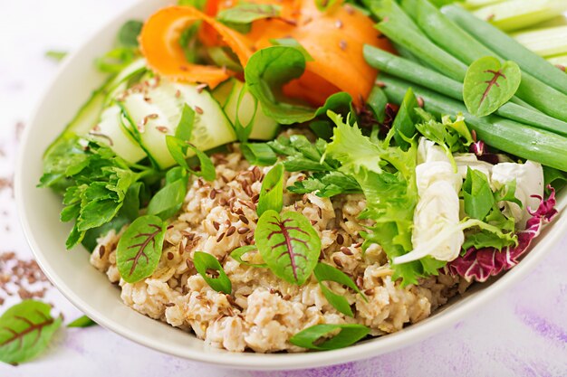 Menu dietetico. Uno stile di vita sano. Porridge di avena e verdure fresche - sedano, spinaci, cetriolo, carota e cipolla sul piatto.